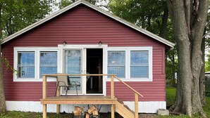 Une petite maison en bois rouge, dotée d’un porche, d’une porte-fenêtre coulissante et d’un escalier menant à l’entrée.