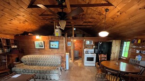 L’intérieur chaleureux d’un chalet avec un plafond en bois, un canapé, une table à manger et un coin cuisine.