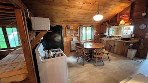 Une cuisine chaleureuse, aménagée dans le style d’un chalet, avec un poêle à bois, une table à manger et des chaises.