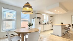 Une cuisine moderne avec des meubles blancs, une table à manger en bois et un luminaire suspendu.