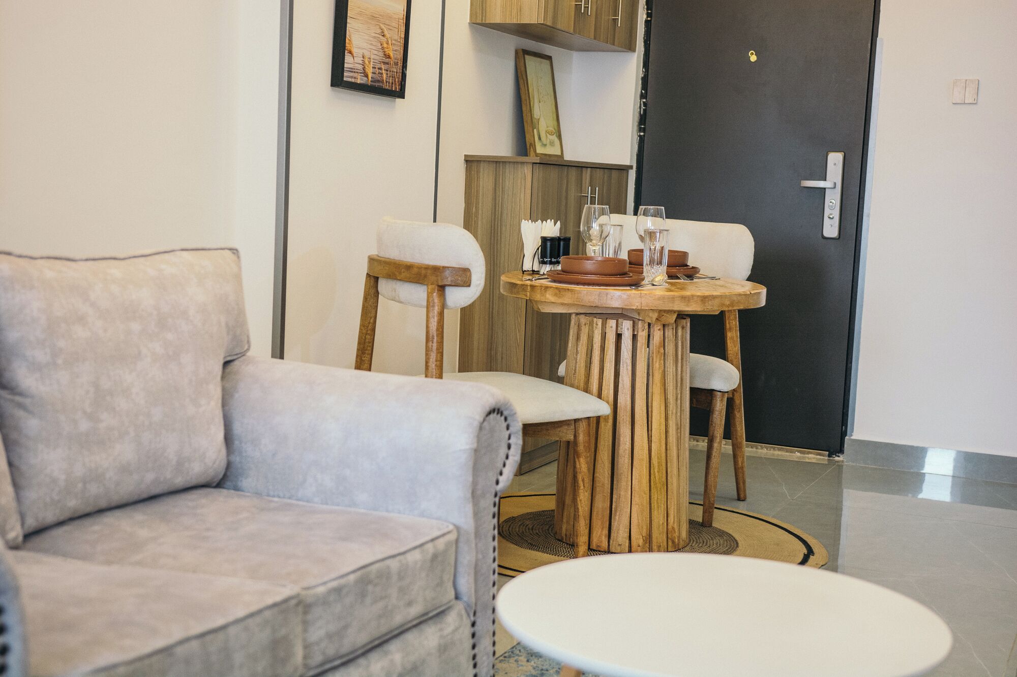 A modern living room with a grey sofa, a wooden dining table with chairs, and a black door in the background.