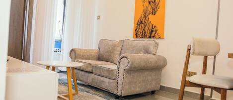 Un salon avec un canapé beige, une chaise en bois, une petite table et un tapis aux motifs bleus et beiges.