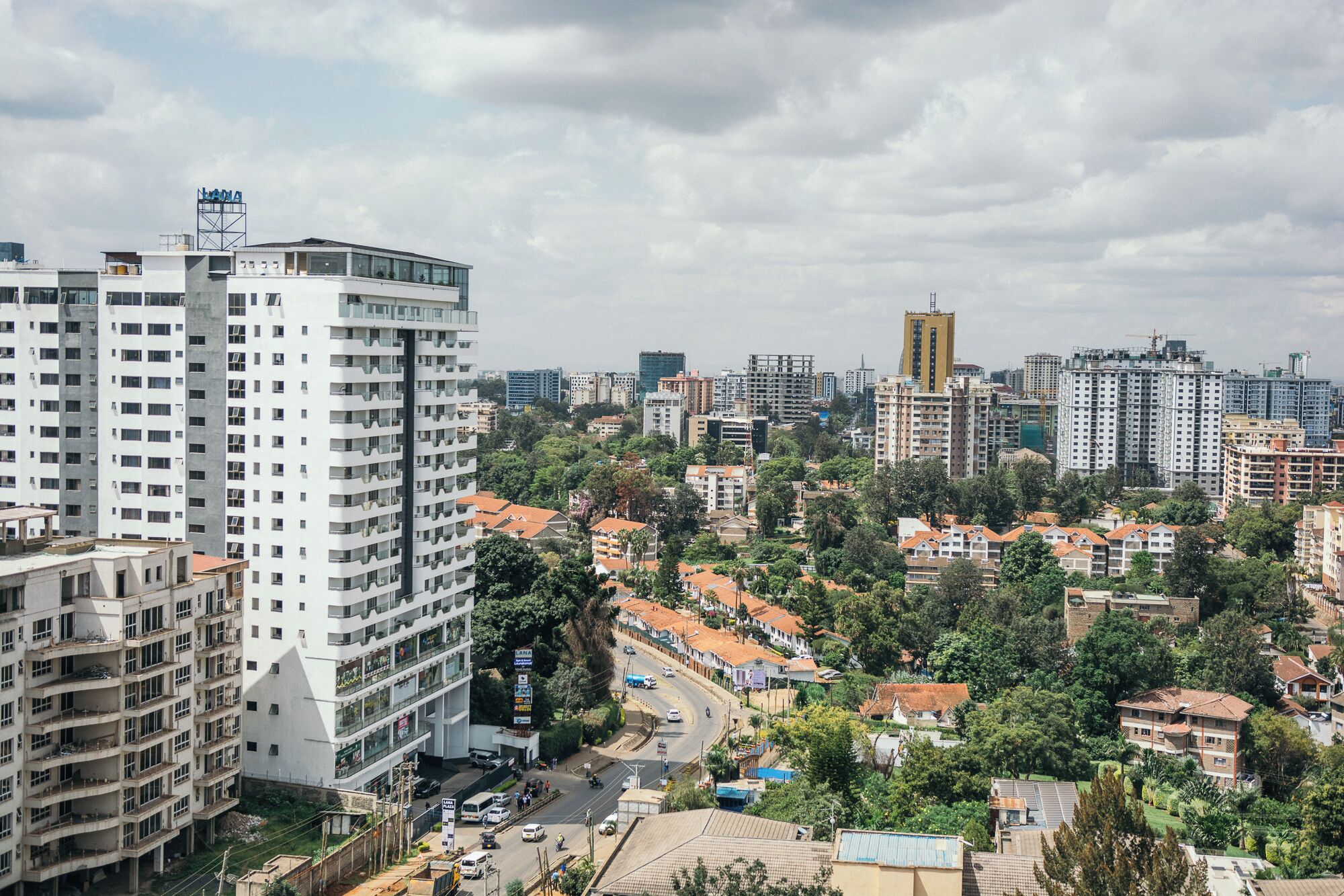 Un immeuble de grande hauteur, doté de nombreux étages et de balcons, entouré d’autres bâtiments et de verdure.