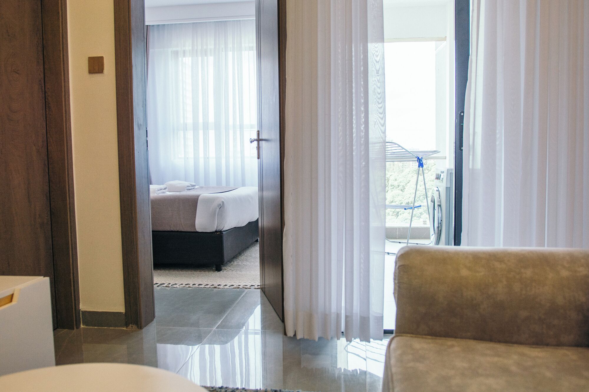 A hotel room with a bed, a chair, and a balcony with a washing machine.