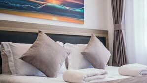Una cama bien hecha con dos almohadas y un edredón doblado, un cabecero de madera y un cuadro de un paisaje marino en la pared.