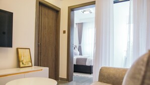 Una habitación de hotel moderna con sofá, una mesita, una puerta de madera y vistas al dormitorio contiguo.