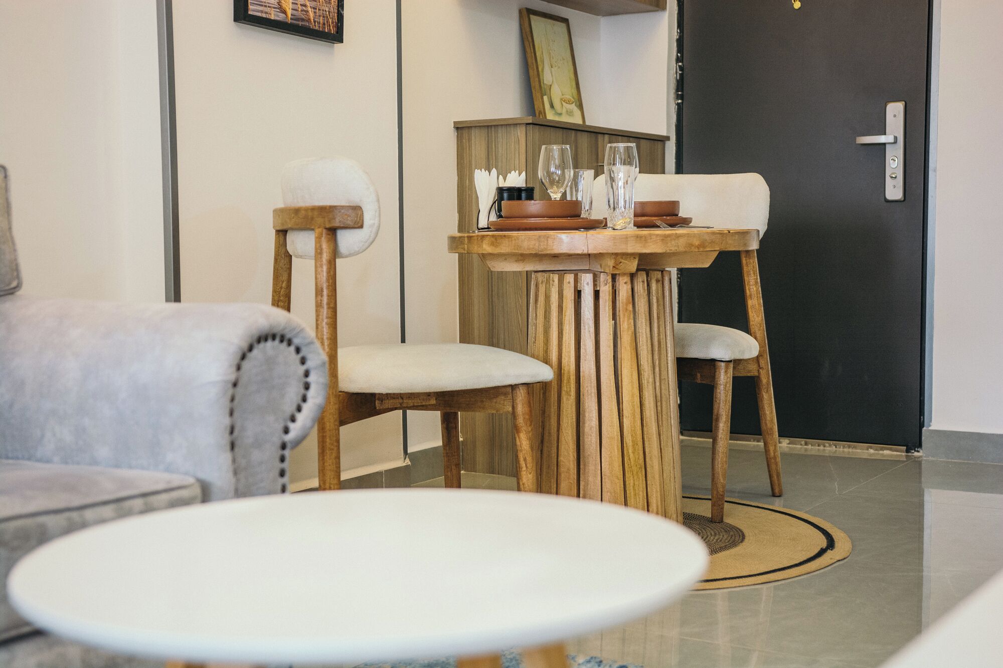 Un rebedor d'hotel modern amb una taula rodona de fusta, dues cadires tapissades i un sofà.