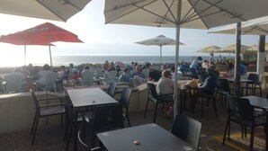 An outdoor seating area with tables and chairs, umbrellas, and a view of the ocean. - Le Cosy Zen des Sables (Mimizan)