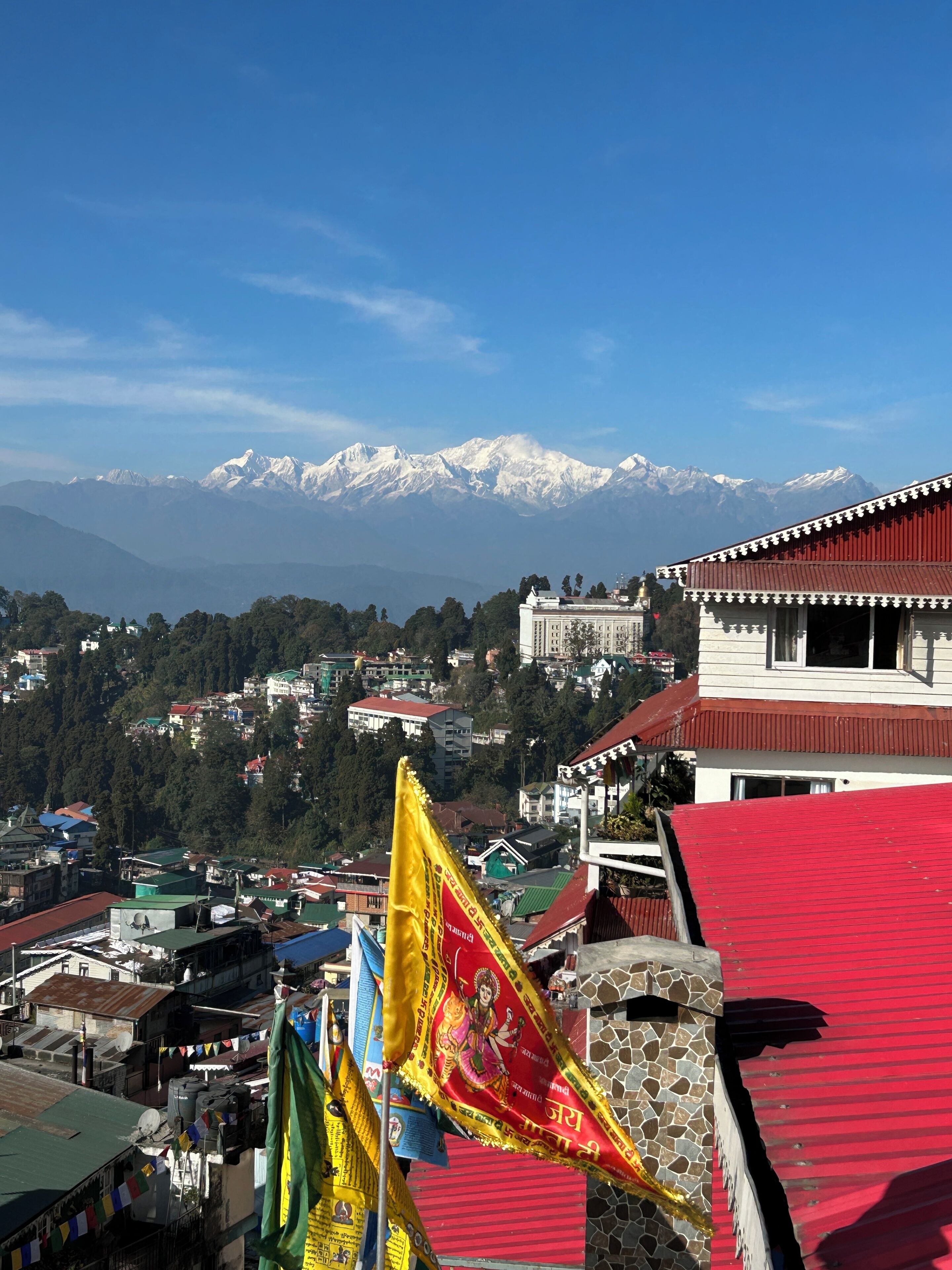 A mountainous landscape with snow-capped peaks in the background, a town with various buildings, and a prominent red-roofed structure in the foreground.