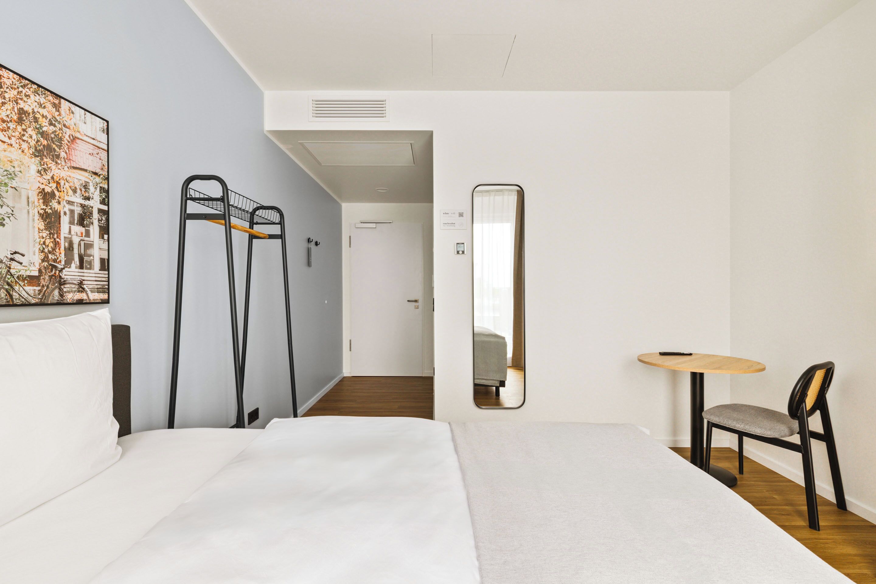Een hotelkamer met een bed, een stoel, een klein tafeltje, een spiegel en een schilderij aan de muur.