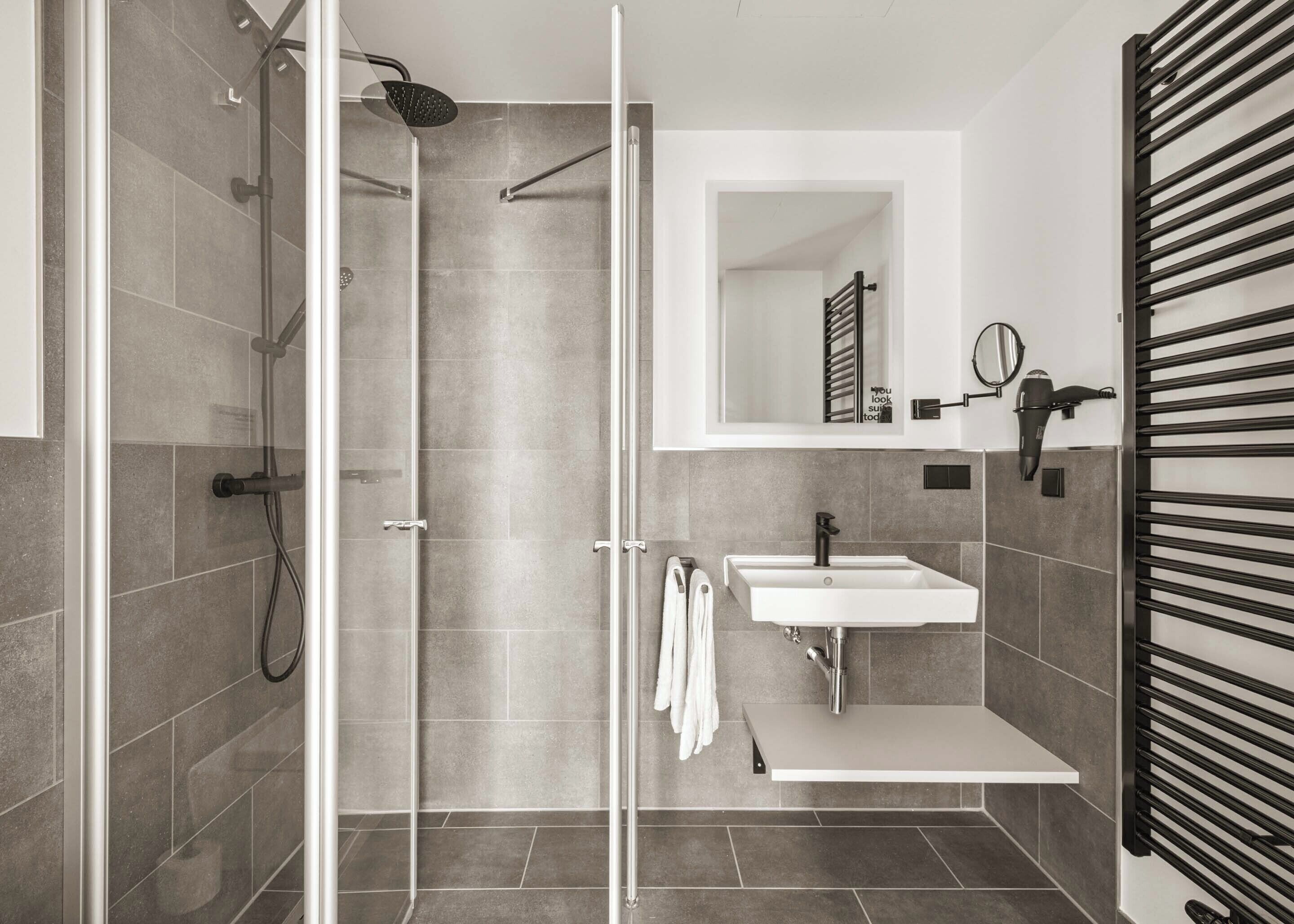A modern bathroom with a glass shower enclosure, a white sink, and a towel rack.