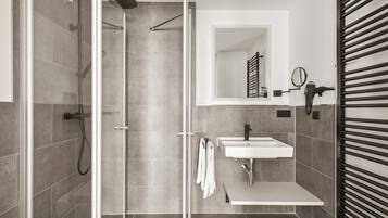 A modern bathroom with a glass shower enclosure, a white sink, and a towel rack.