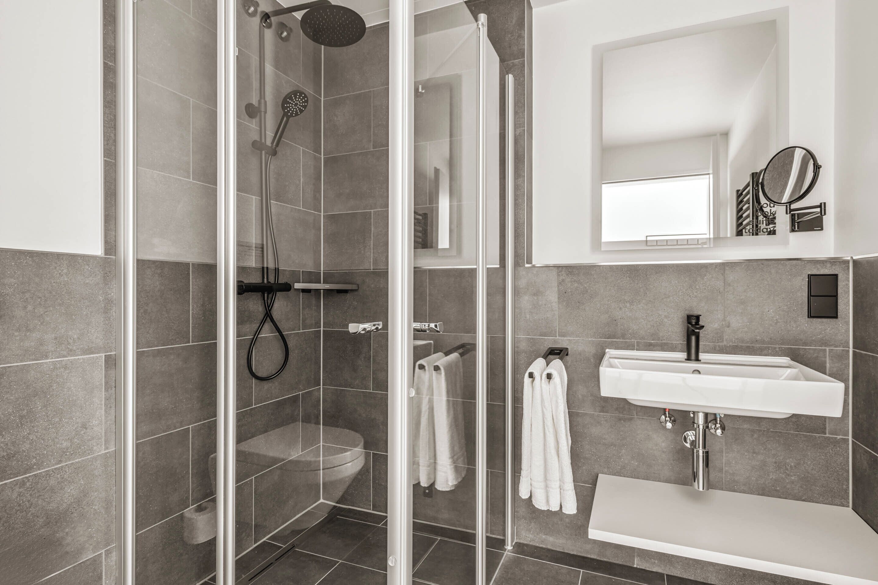 Une salle de bain moderne avec une douche à parois de verre, des toilettes et un lavabo surmonté d’un miroir.