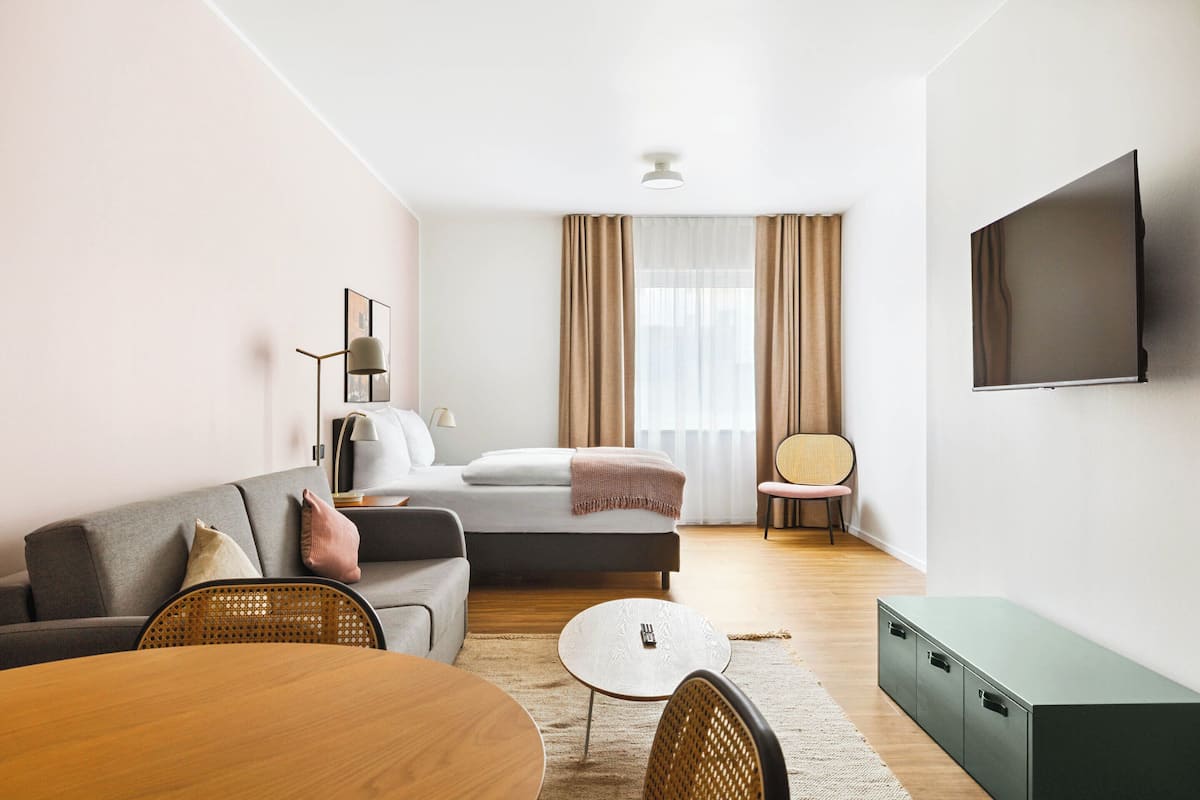 Ein modernes Wohnzimmer mit einer Couch, einem Esstisch, einem Fernseher und einem Fenster mit Vorhängen.