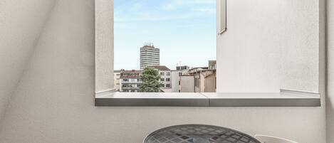Un balcón con una mesa y sillas, vista a un paisaje urbano y un edificio al fondo.
