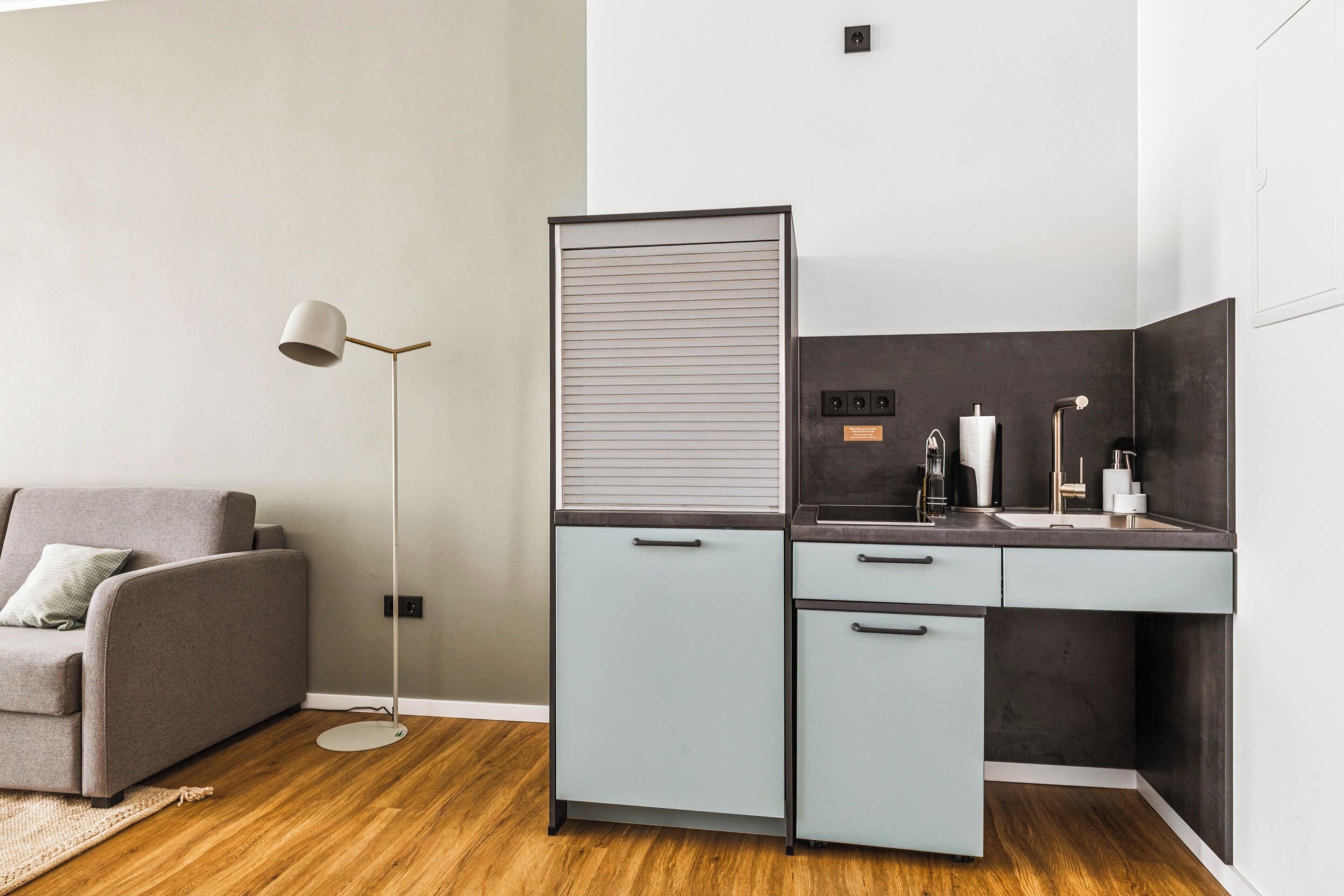 A modern kitchen with a grey cabinet, a built-in sink, and a floor lamp.