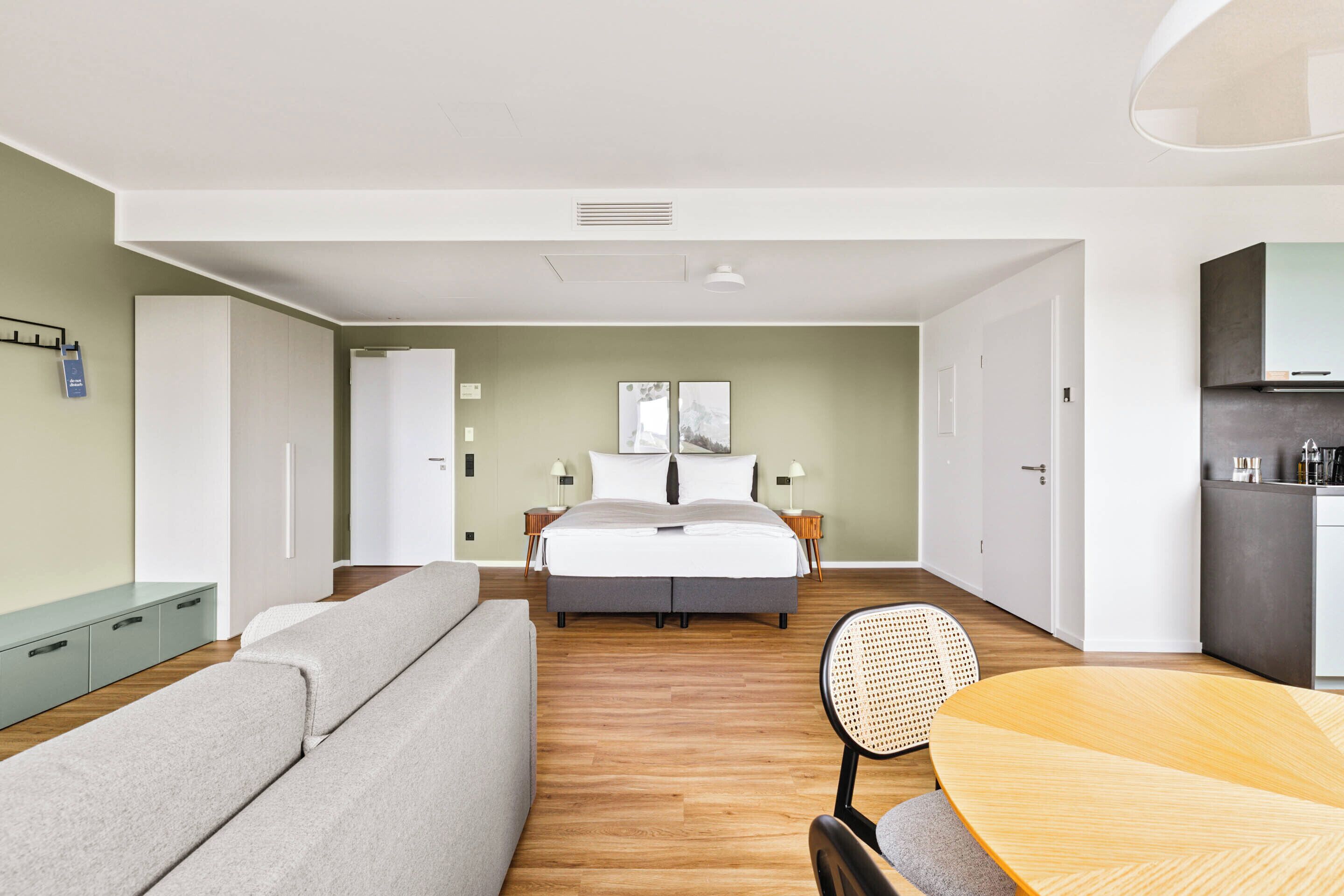 Ein modernes Hotelzimmer mit Bett, einer Couch, einem Esstisch und einer Küchenzeile.