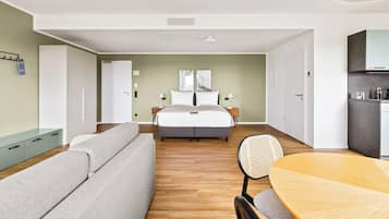 Ein modernes Hotelzimmer mit Bett, einer Couch, einem Esstisch und einer Küchenzeile.