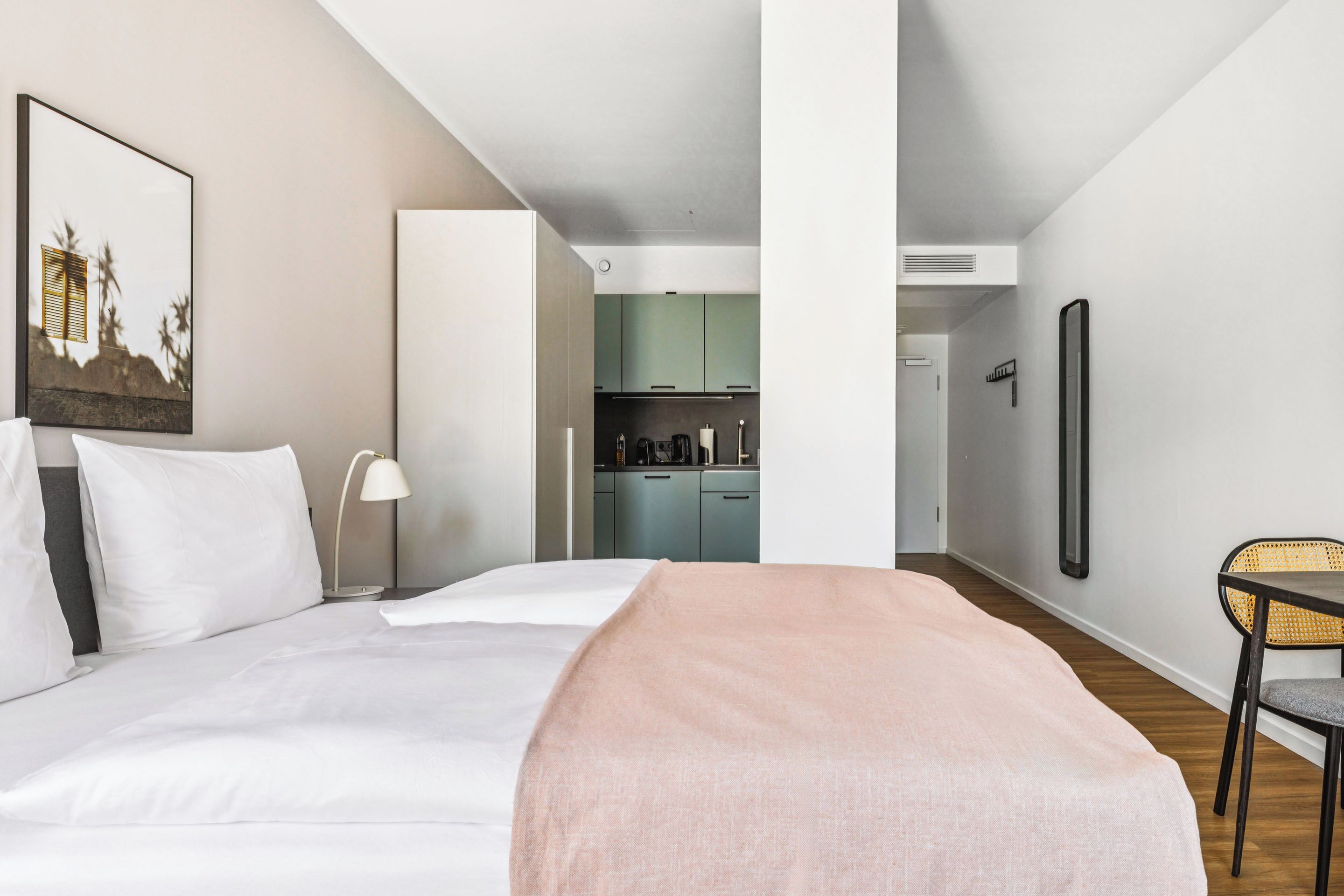Habitación de hotel moderna con una cama grande, una mesita de noche, una lámpara, una silla y vistas al área de la cocina.
