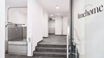 A modern hotel interior with a glass elevator, a staircase, and a wall with the text "Designed to Stay".