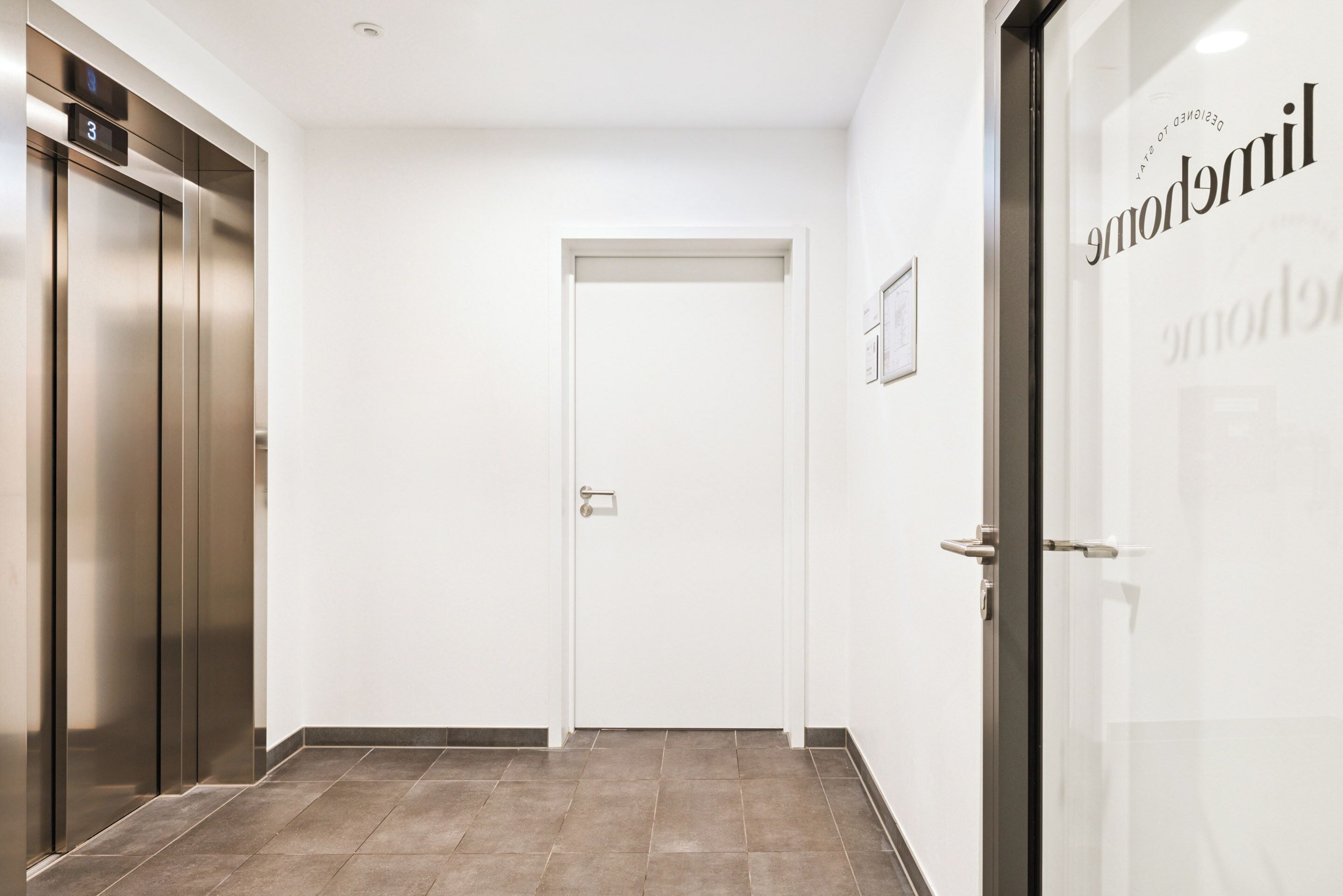 A hallway with an elevator, a door, and a glass wall with the word "Milomobile" on it.