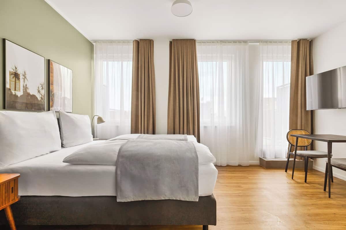 Ein Hotelzimmer mit Bett, Schreibtisch, Sessel und Fernseher.