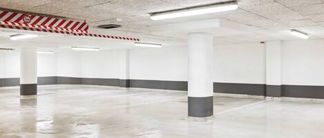 A spacious indoor parking area with concrete floors and white walls, featuring several pillars and overhead fluorescent lighting.