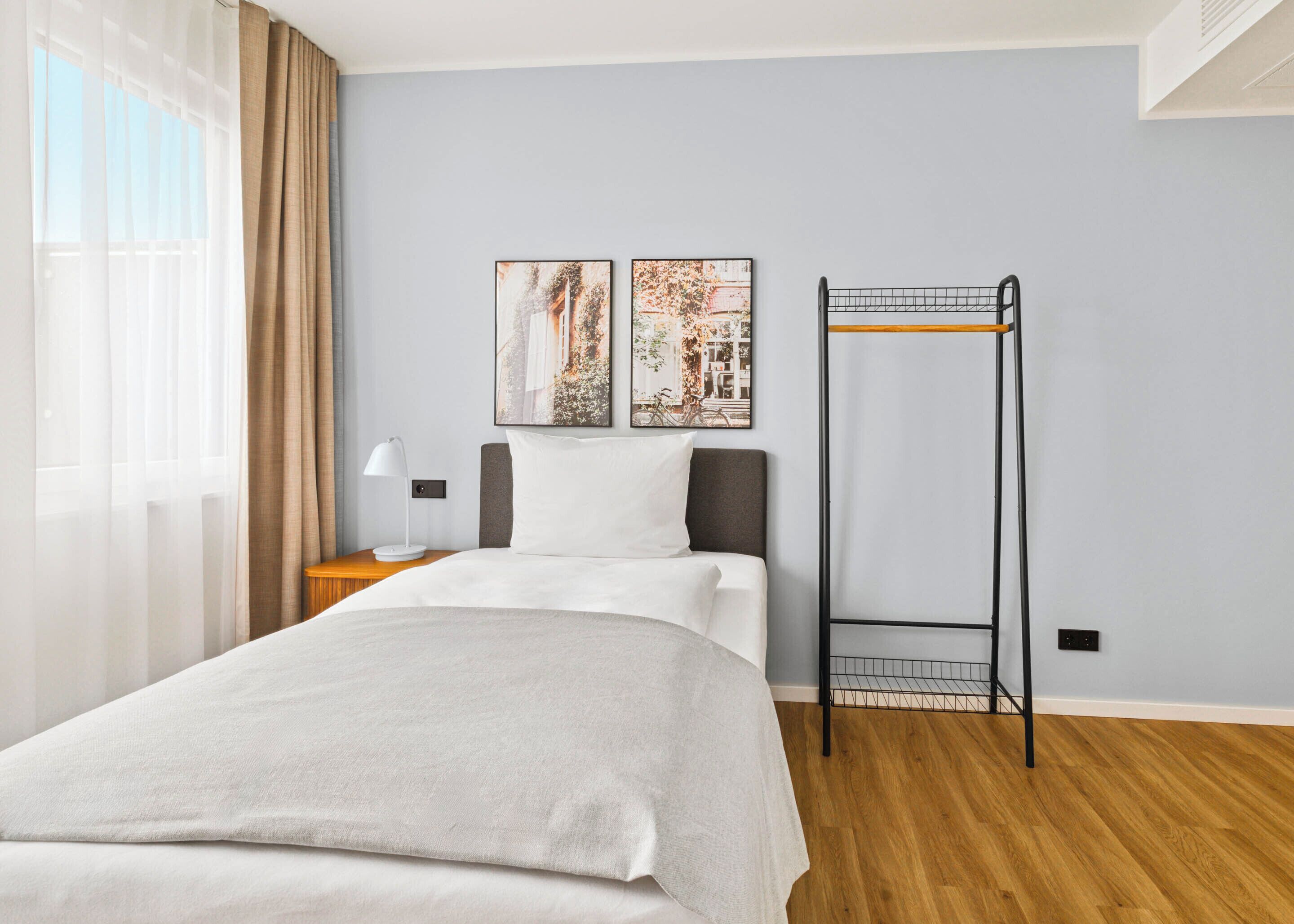 A hotel room with a bed, a bedside table with a lamp, a wall-mounted picture, and a pull-out shelf.