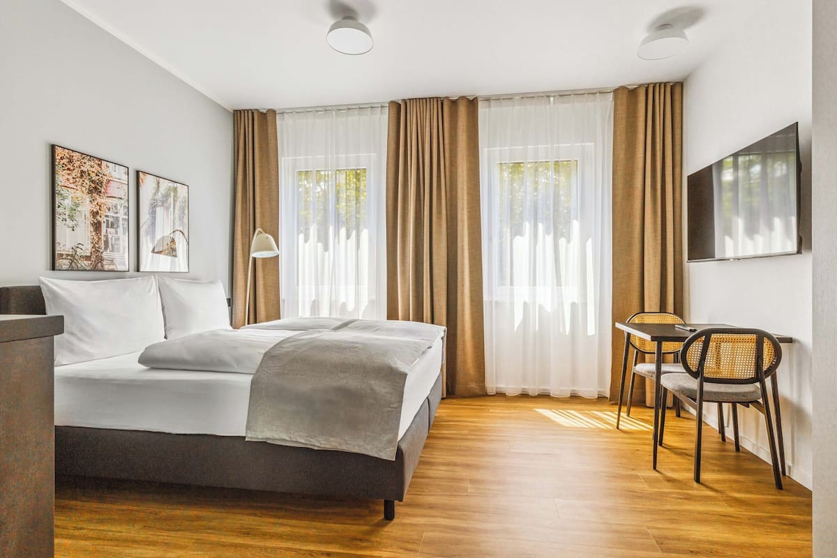 Ein Hotelzimmer mit einem Bett, einem Schreibtisch, zwei Stühlen, einem Fernseher und Bildern an der Wand.