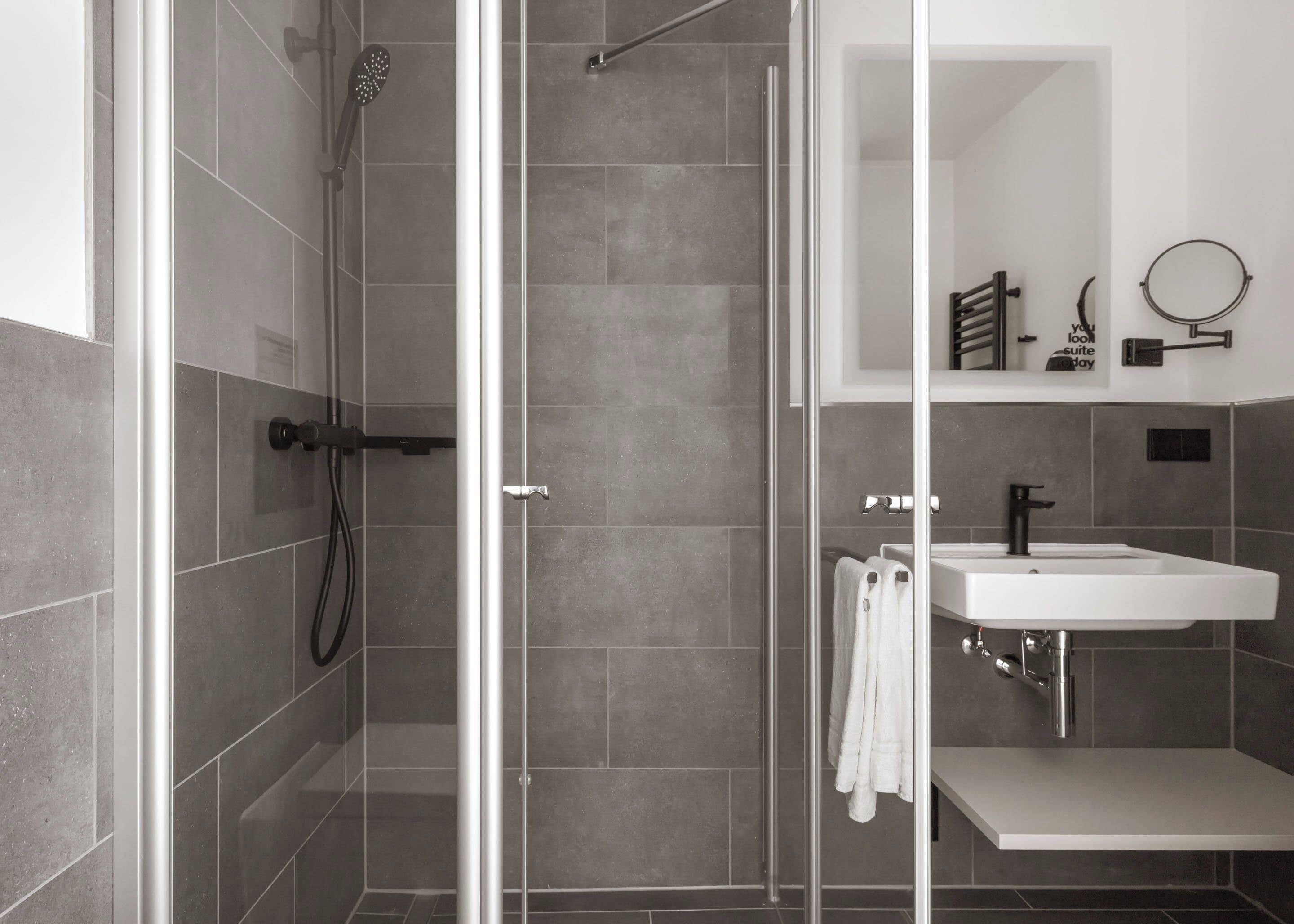 A modern bathroom with a glass-enclosed shower, a white sink, and a mirror.