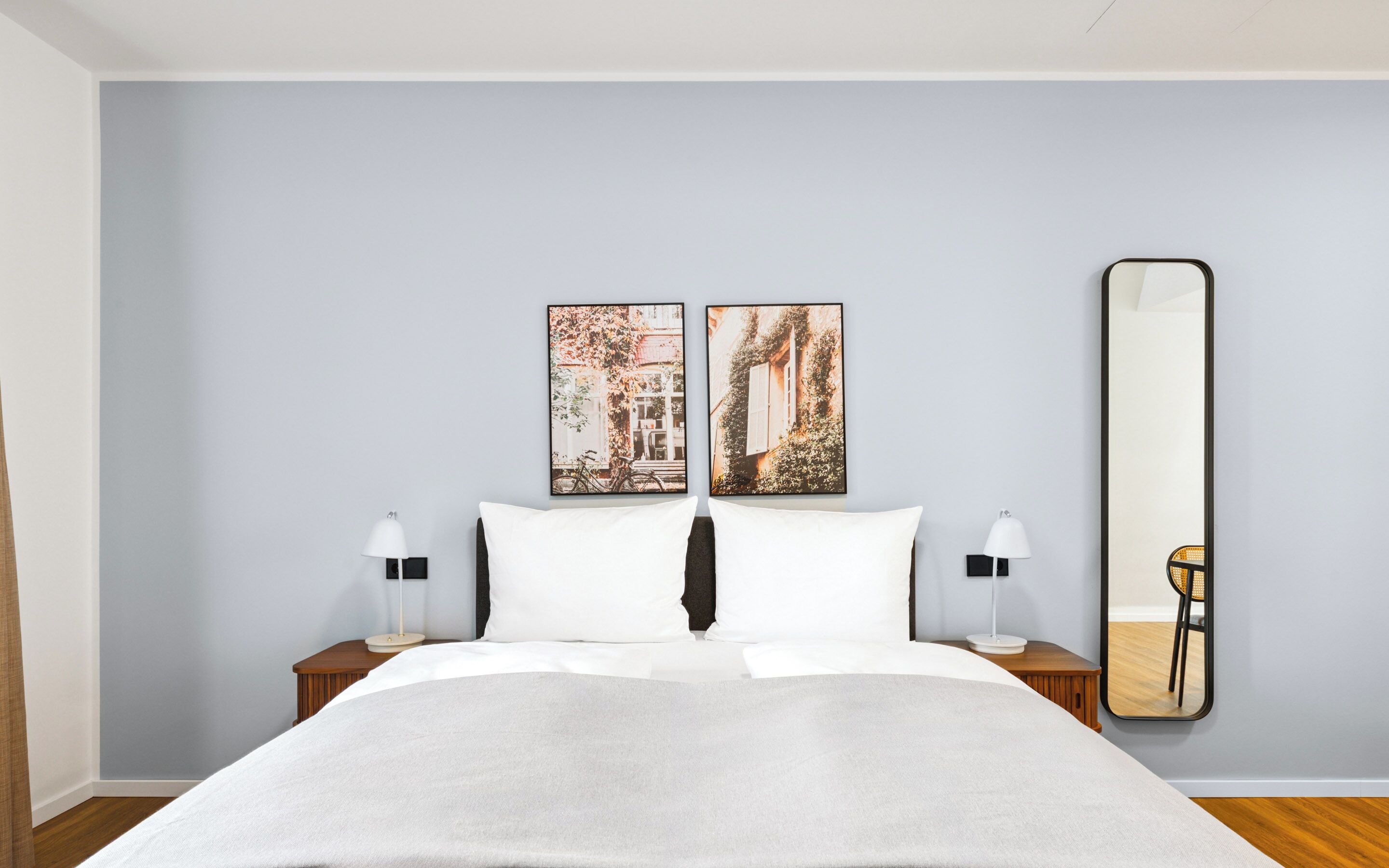 A hotel room with a bed, two nightstands, two wall-mounted lamps, and two framed pictures above the bed.