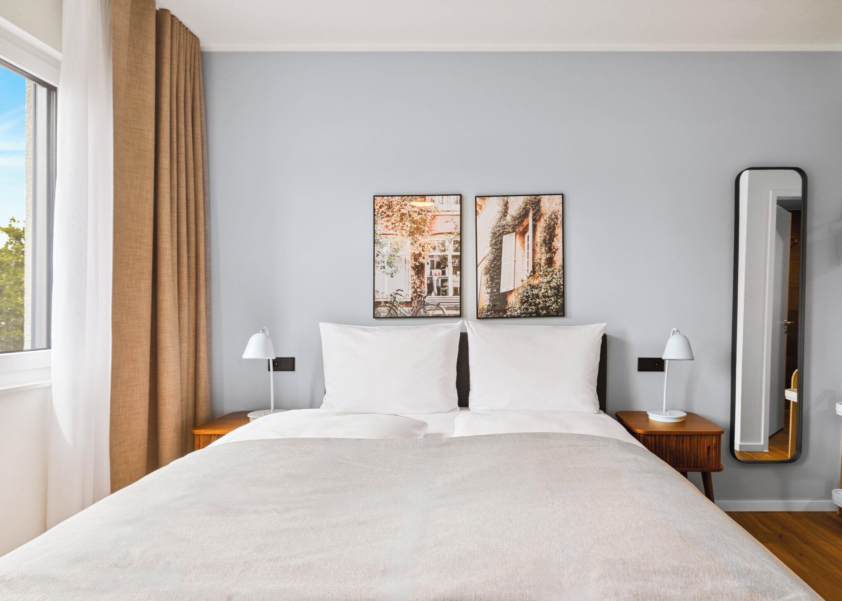 A hotel room with a large bed, two bedside tables with lamps, a large mirror, and two framed pictures on the wall.