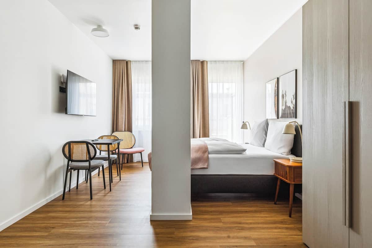 Ein modernes Hotelzimmer mit einem Bett, einem Schreibtisch, einem Sessel und einem an der Wand befestigten Fernseher.