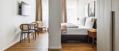 Una habitación de hotel moderna con cama, escritorio, silla y televisor en la pared.
