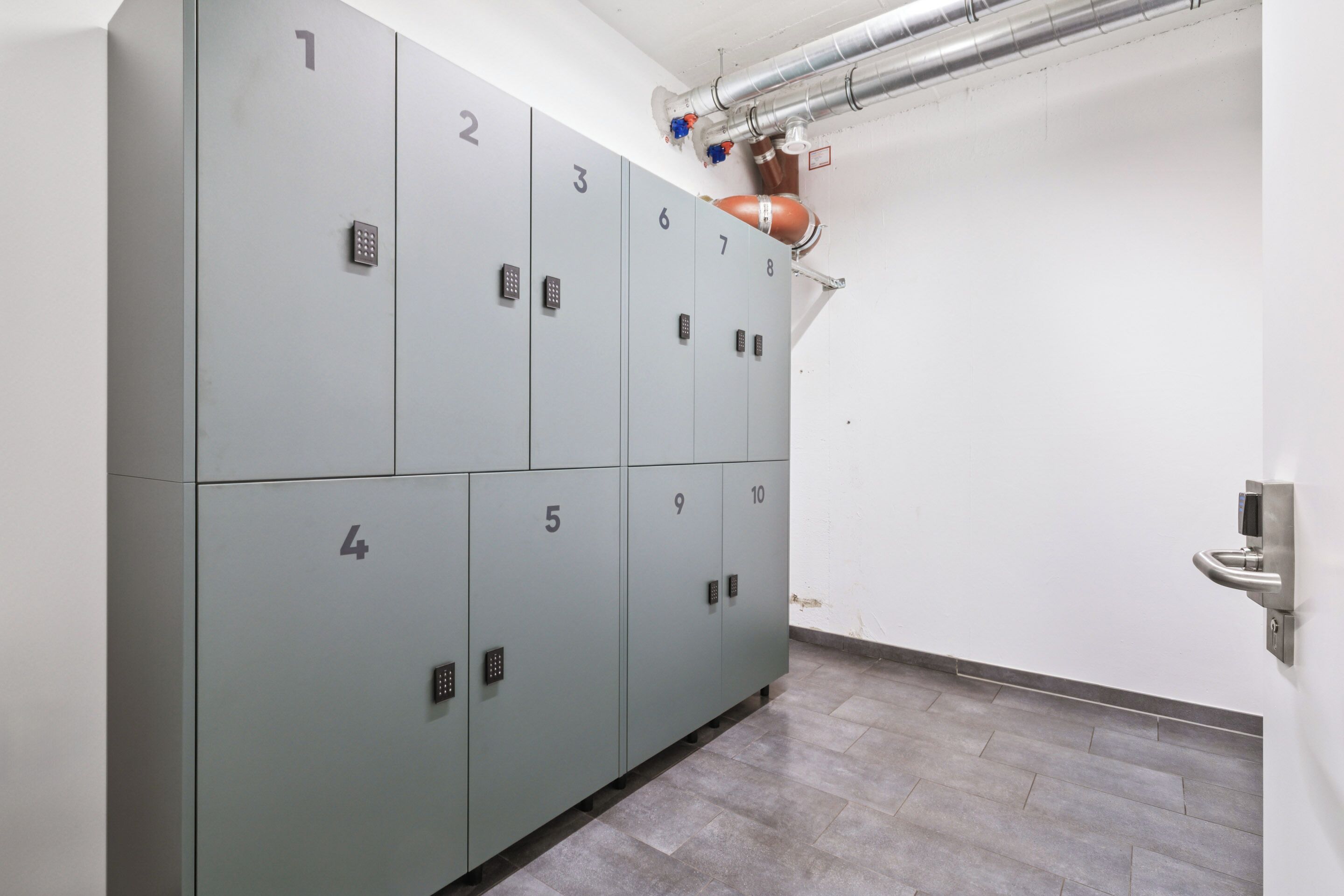A row of grey lockers numbered 1 to 10, with a ventilation system above and a wall-mounted sensor on the right.