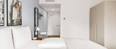 A modern hotel room with a large bed, a bedside table, a lamp, and a wardrobe.