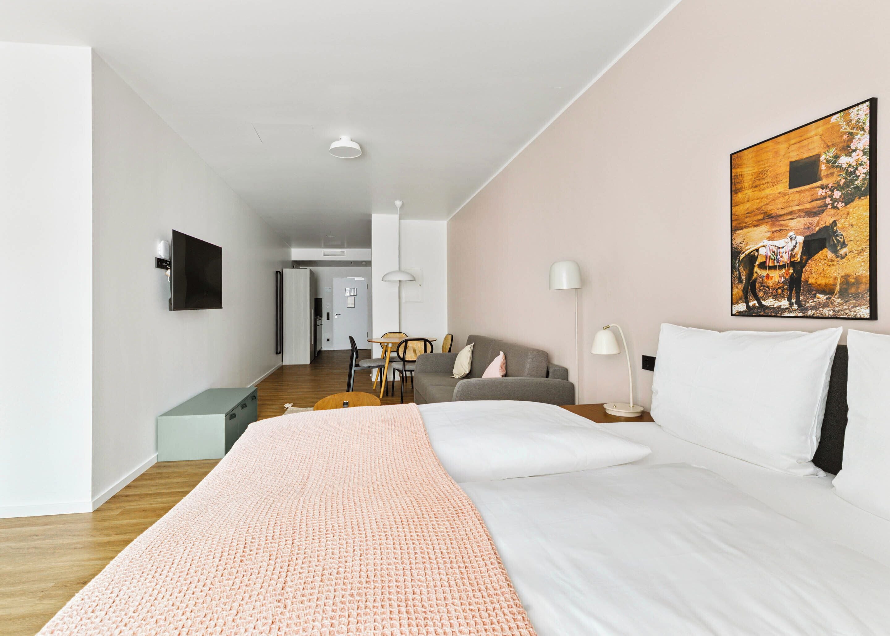Ein modernes Hotelzimmer mit einem großen Bett, einem Essbereich, einer Couch und einem an der Wand montierten Fernseher.