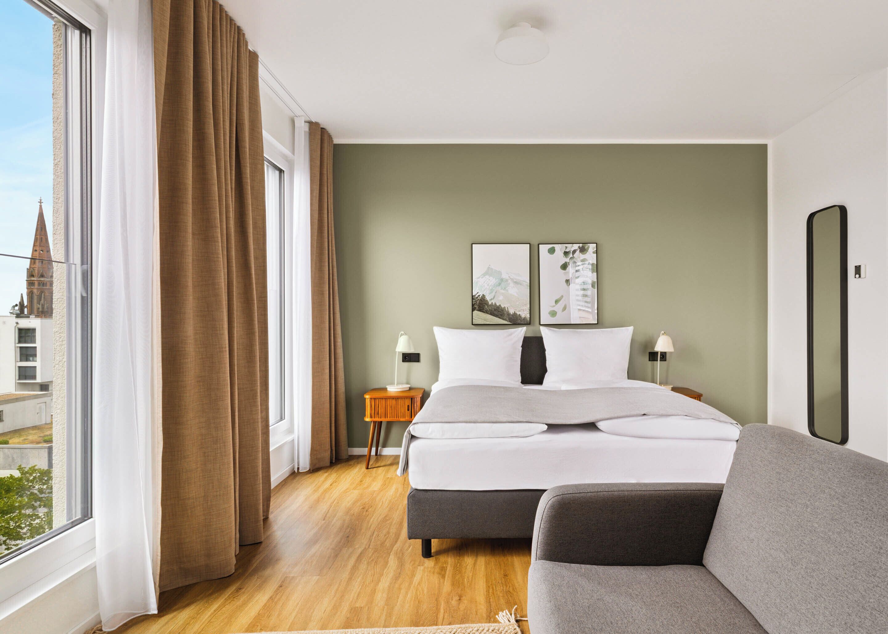 A hotel room with a bed, a sofa, a nightstand, and a view of a building.