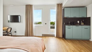 A bedroom with a bed, a TV, a desk, and a kitchenette. - Limehome Bochum Kortumstr. (Bochum)