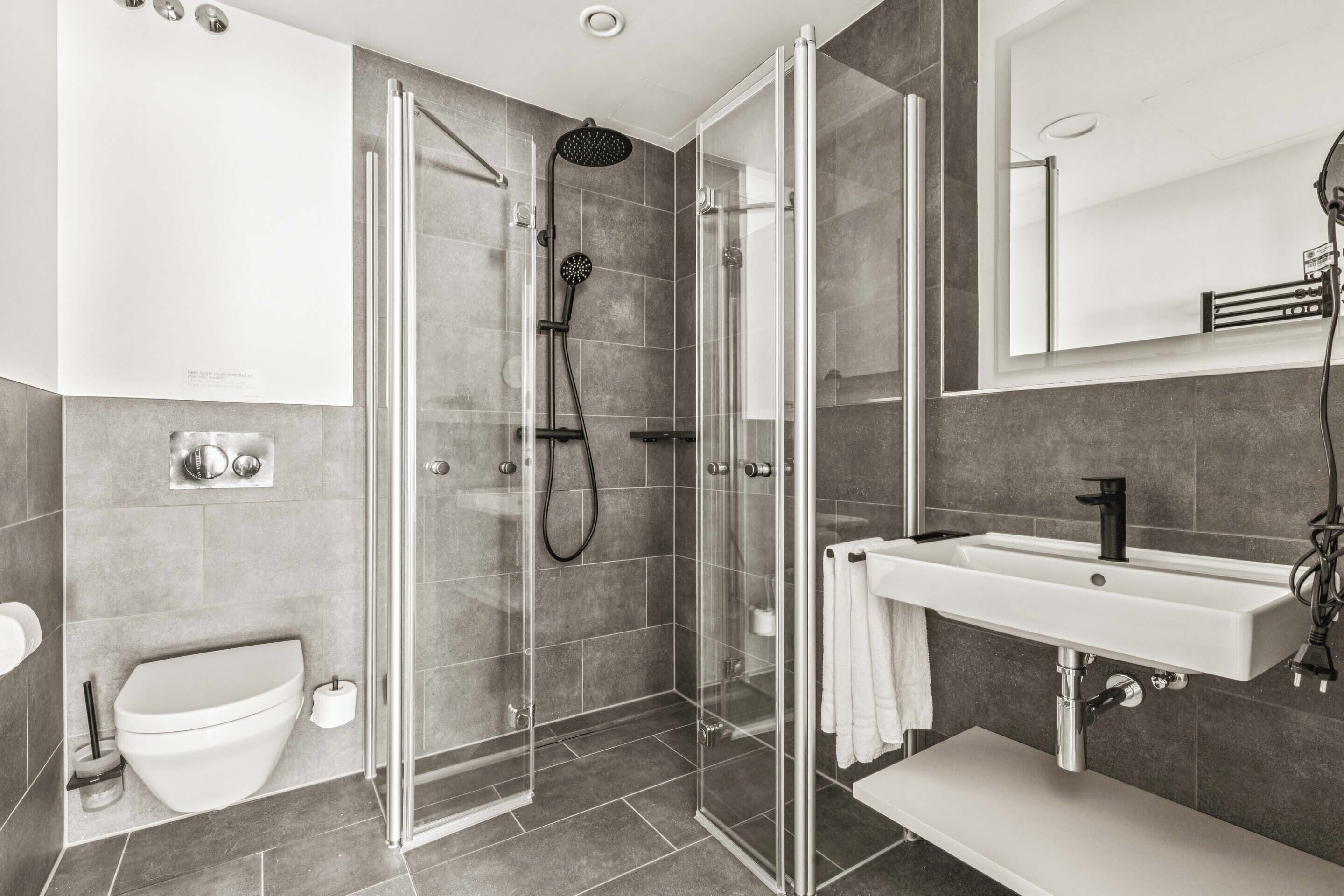 Un baño moderno con ducha de vidrio, un lavamanos blanco y un inodoro.