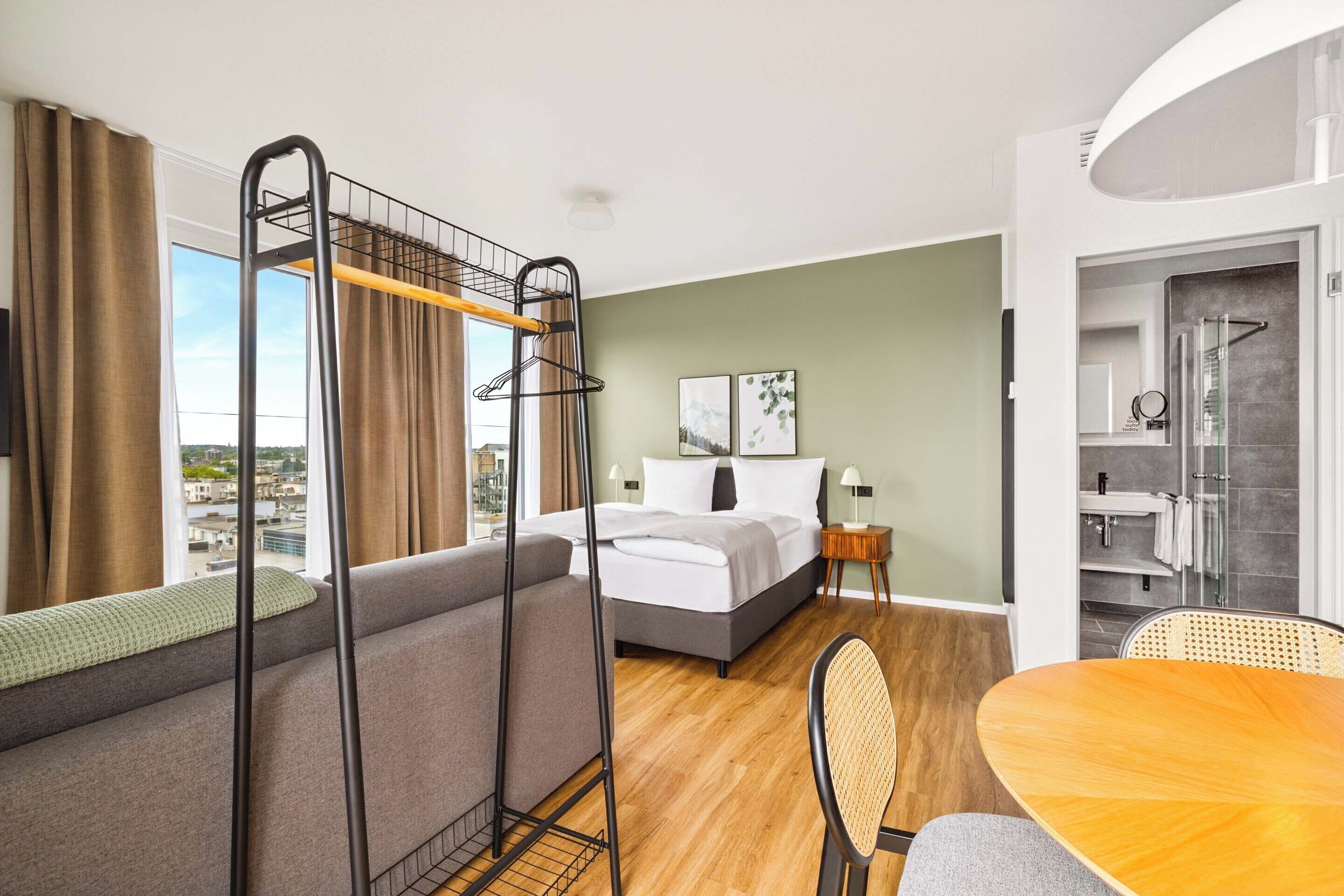 A hotel room with a bunk bed, a sofa, a dining table, and a bathroom visible through an open door.