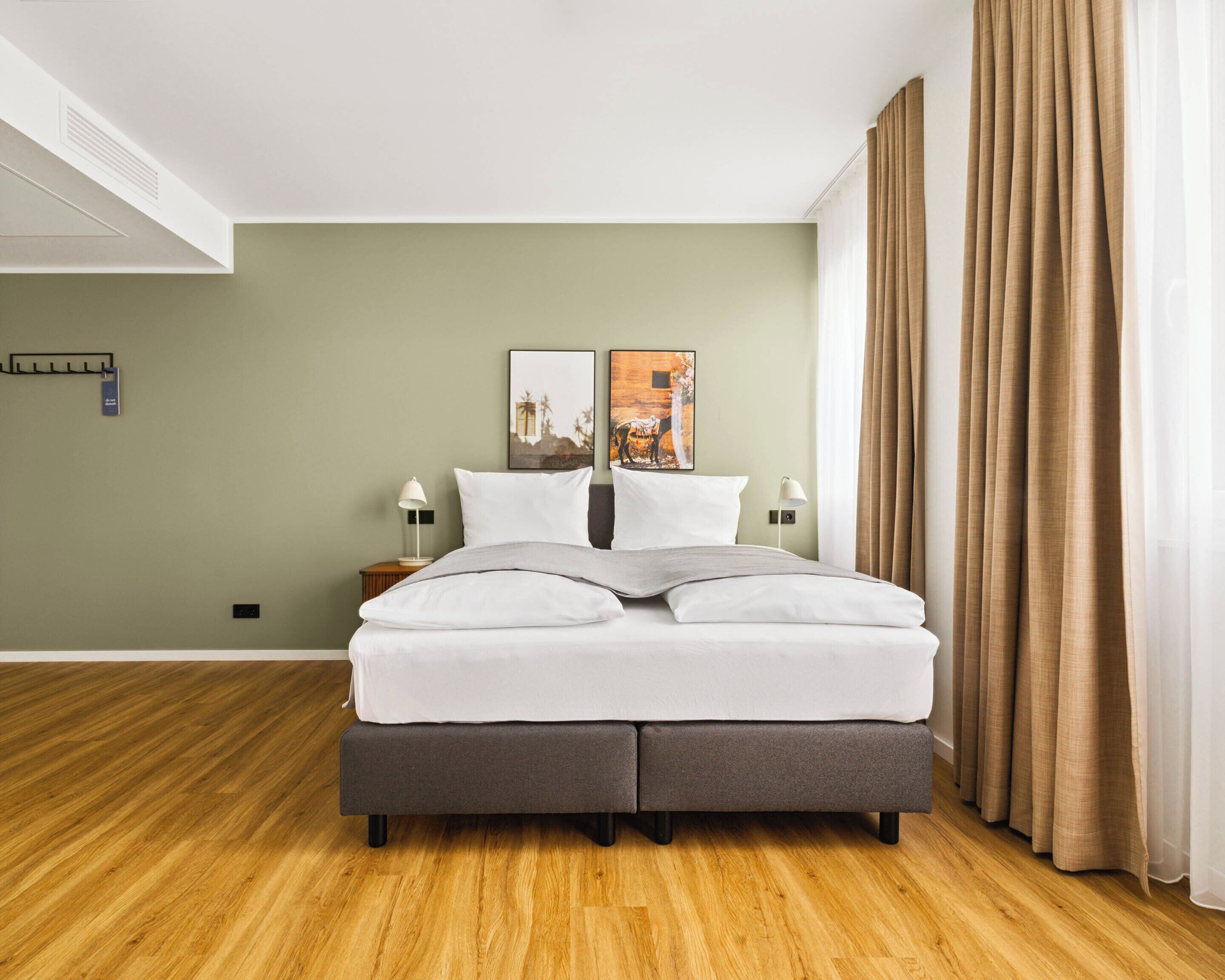Une chambre d’hôtel moderne avec un grand lit, deux tables de chevet avec des lampes, une tête de lit et des œuvres d’art accrochées au mur.