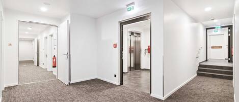 Un pasillo moderno de hotel con pisos alfombrados, paredes blancas y puertas que dan a las habitaciones.