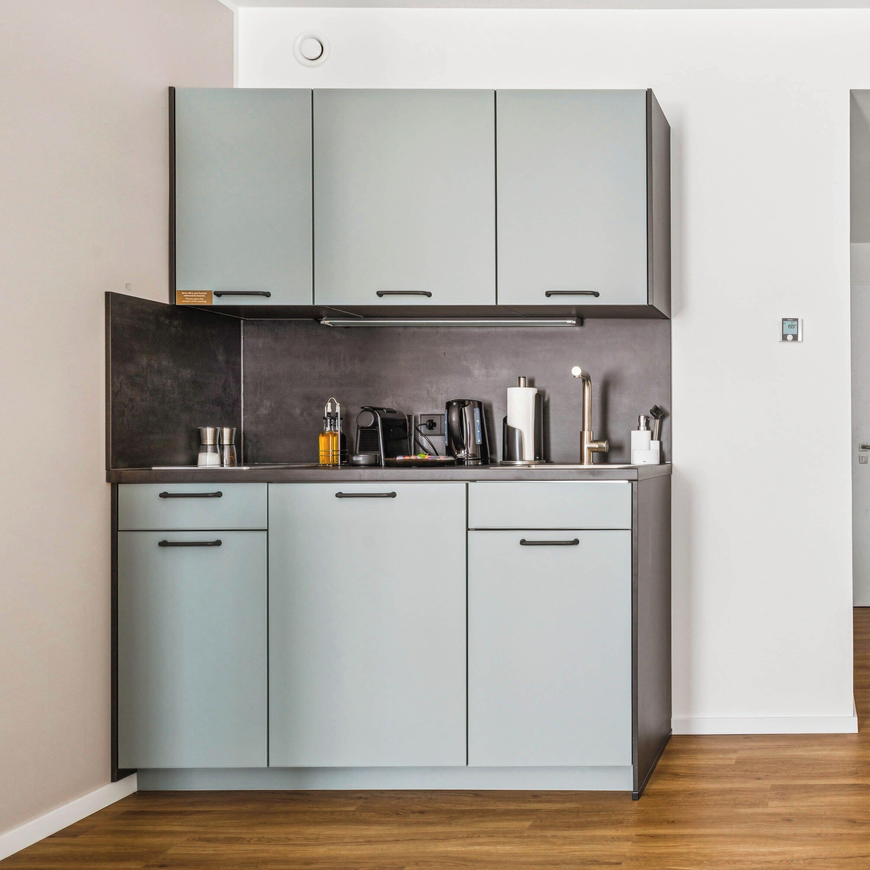 A modern kitchen with grey cabinets, a stainless steel countertop, and various appliances.