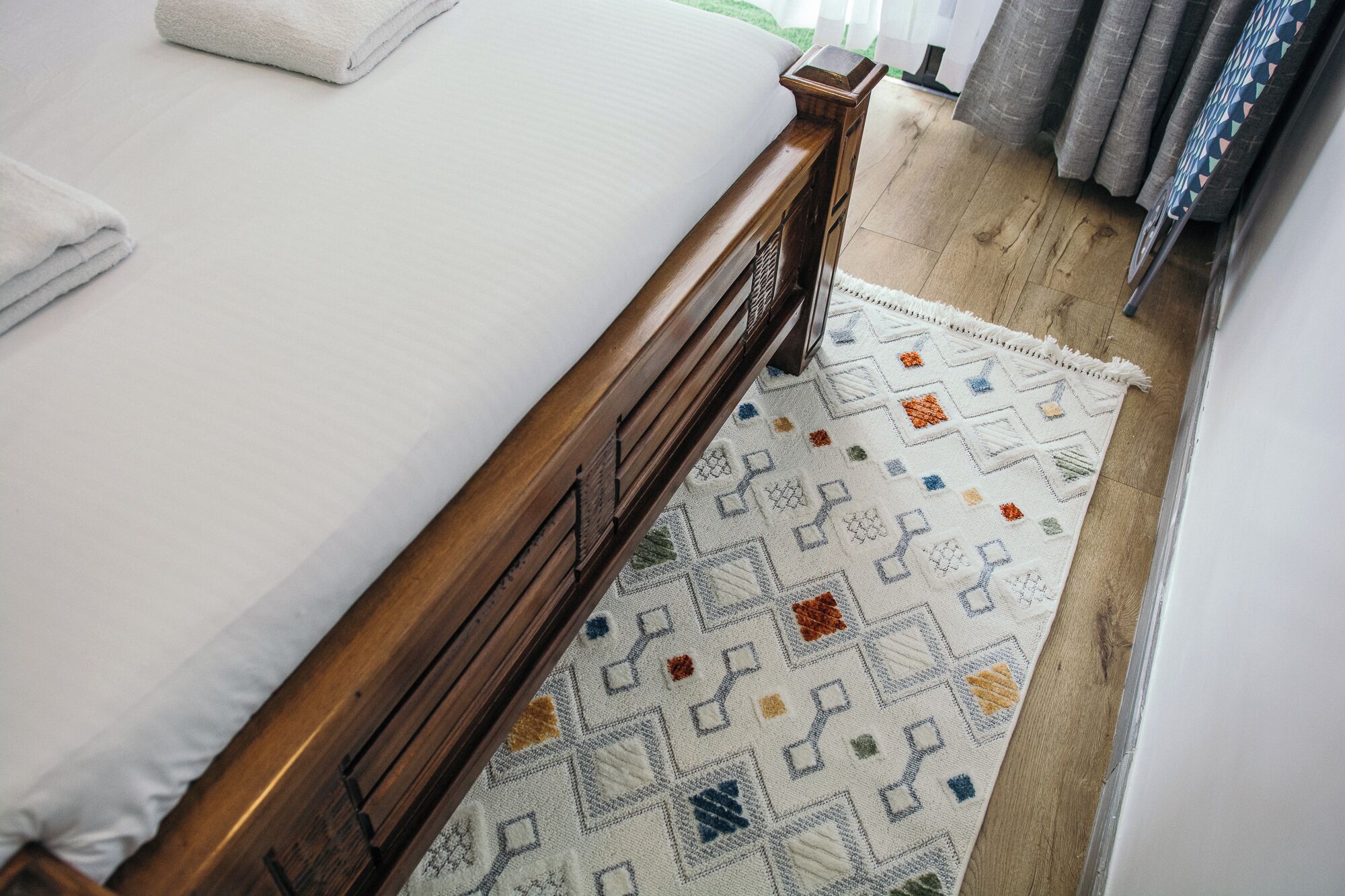 Ein Bett mit Holz-Kopfteil, einer weißen Matratze und einem gemusterten Teppich auf dem Boden.