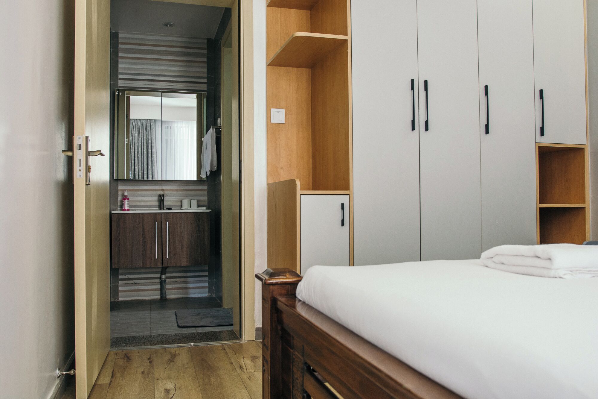 Une chambre à coucher avec un lit en bois, une armoire intégrée et une salle de bain équipée d’un lavabo et d’un miroir.
