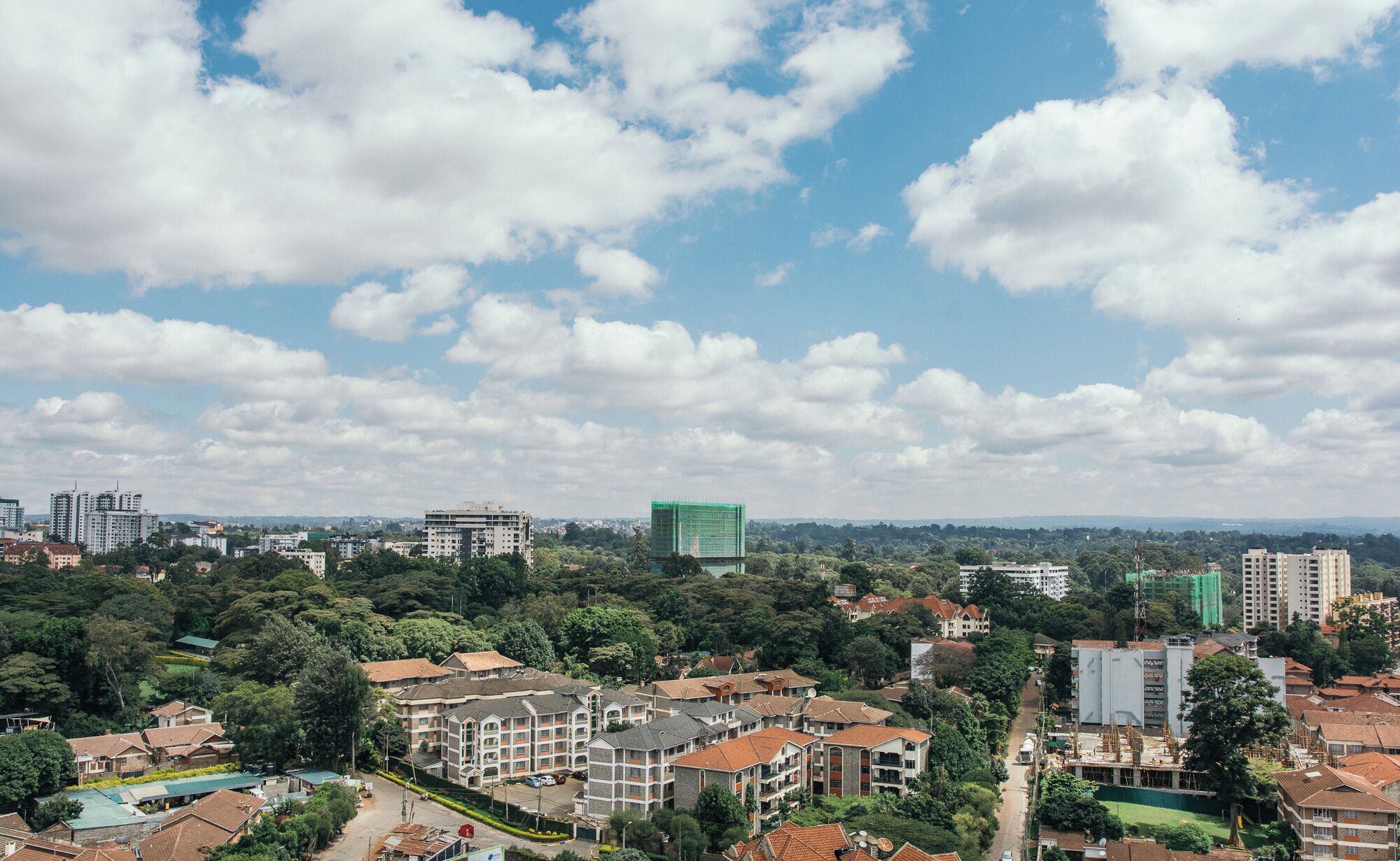 Un quartier résidentiel composé d’immeubles à plusieurs étages, où se côtoient des bâtiments résidentiels et commerciaux, et où le ciel est dégagé, parsemé de quelques nuages.