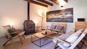 Un salon chaleureux, meublé de meubles en osier, avec une cheminée et un tableau représentant un paysage au bord de la rivière.