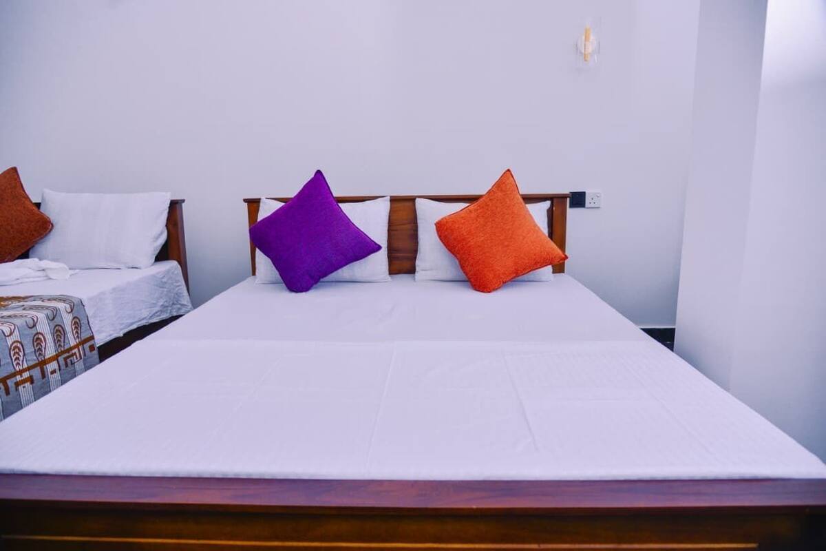 A double bed with white bedding and two pillows, one purple and one orange, in a room with a wooden headboard.