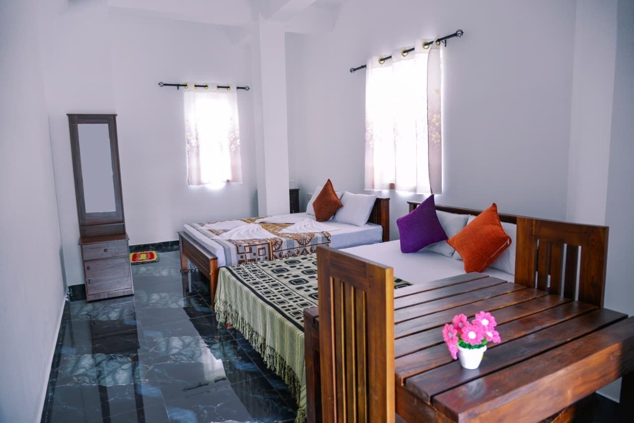 A bedroom with two beds, a wooden table, a mirror, and a window with curtains.